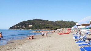 A beach with sun loungers and umbrellas, a rocky shoreline, and a hill in the background. - Lucerna Due by Interhome (Ameglia)