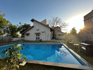 Ein modernes Haus mit Swimmingpool, einer Terrasse und Gartenmöbeln, und einem wolkenlosen Himmel.