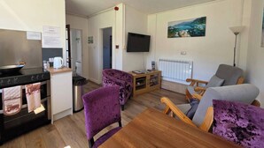 A compact living space with a kitchenette, a dining area, a sofa, a TV, and a painting on the wall. - Cosy Apartment That Sleeps 3, Pets Welcome (Garve)