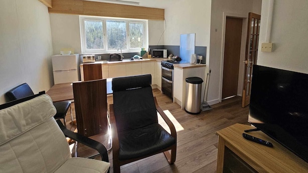 A compact living space with a kitchenette, a dining area with a table and chairs, a TV, and a trash bin. - Cosy Apartment That Sleeps 3, Pets Welcome (Garve)