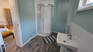 A bathroom with a glass shower enclosure, a sink, and a wooden floor. - Cosy Apartment That Sleeps 3, Pets Welcome (Garve)