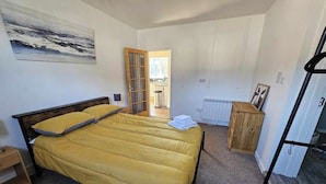 A bedroom with a bed, a wooden cabinet, a radiator, and a door leading to another room. - Cosy Apartment That Sleeps 3, Pets Welcome (Garve)
