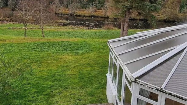 Et hus med skråt tag og udsigt over et grønt område og et mindre vandareal.