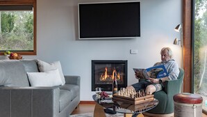 Ein Wohnzimmer mit grauem Sofa, Kamin, Flachbildfernseher und einer Person, die ein Buch liest.
