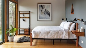 Ein Schlafzimmer mit einem Bett, einer Topfpflanze, einer hölzernen Bank und einem gerahmten Kunstwerk an der Wand.