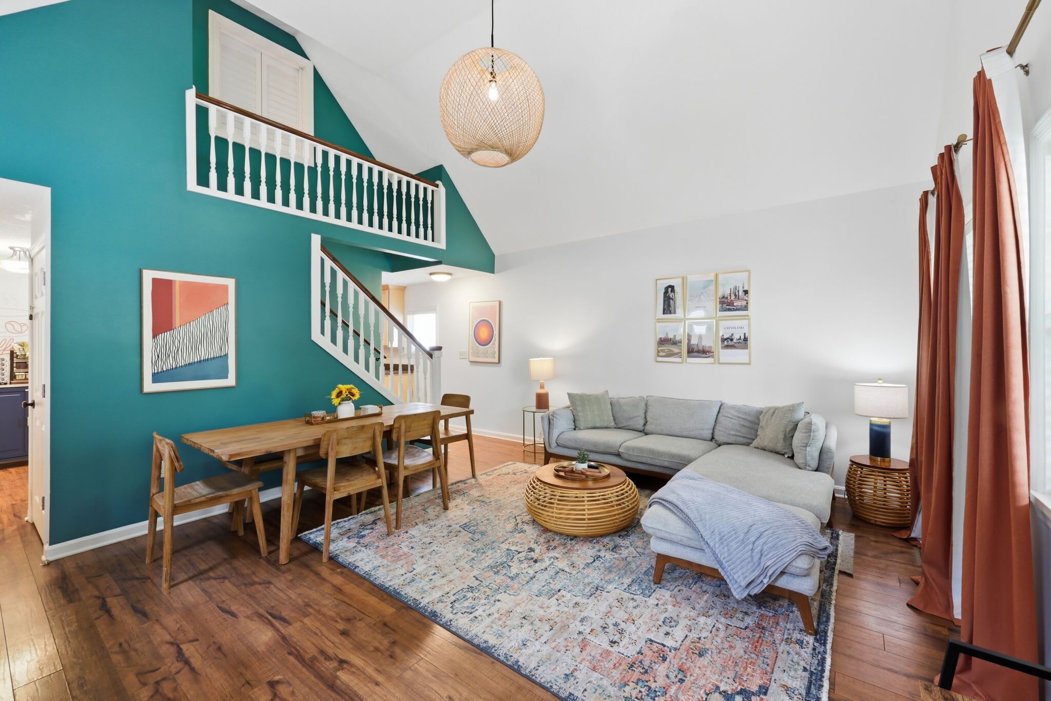 Una sala de estar moderna con una pared de acento color turquesa, piso de madera, una escalera, un comedor y un sofá.