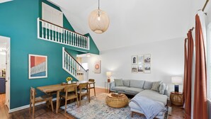 A modern living room with a teal accent wall, wooden flooring, a staircase, a dining area, and a sofa. - Coffee Lover's Paradise - Heart of Tremont (Cleveland)