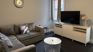 A modern living room with a sofa, a coffee table, a TV on a stand, and a wall clock. - Oxford-house-sleeps 7-parking-garden (Oxford)