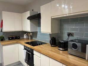 Una cocina moderna con armarios blancos, encimera de madera, campana extractora negra, una tetera, un tostador y una lavadora.
