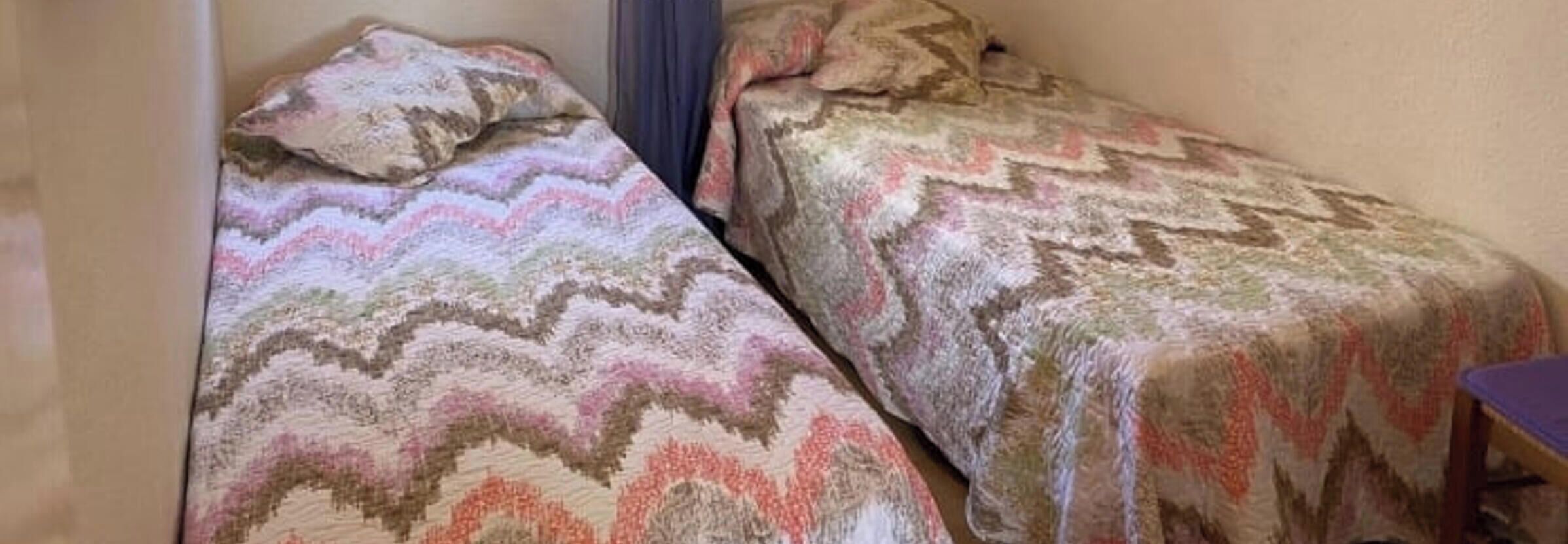Twee bedden met beddengoed met een patroon in een kamer met effen muren.