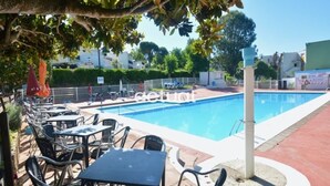 Una piscina amb gandules i taules, envoltada per una tanca i vegetació.