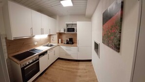 Pieni, käytännöllinen keittiö, jossa on valkoiset kaapit, mikroaaltouuni, liesi ja pesuallas. Lattialla on puulattia ja seinällä taulu.