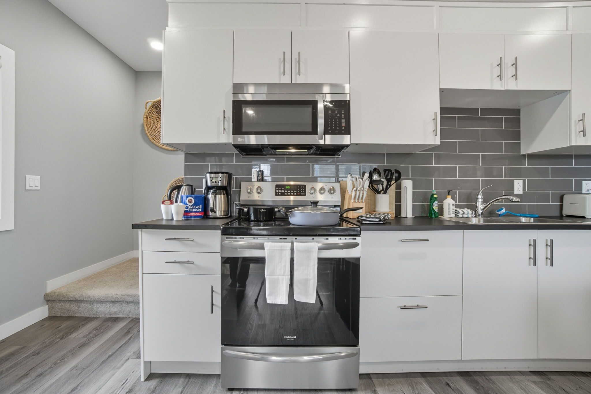 Een moderne keuken met roestvrijstalen apparatuur, witte kasten en een grijze betegelde achterwand.