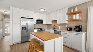 Una cocina moderna con armarios blancos, electrodomésticos de acero inoxidable, una isla de madera y taburetes de bar.