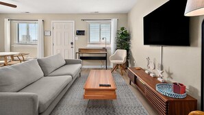 Una sala de estar con sofá, mesa de centro, televisor y un pequeño comedor con mesa y sillas.