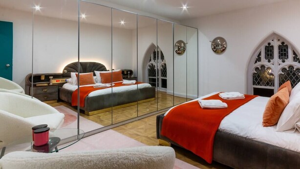 Een moderne slaapkamer met een grote spiegel, twee bedden, een kaptafel en een rode accentmuur.