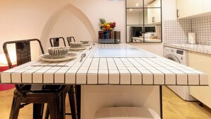 Een moderne keuken met een betegelde aanrecht, zwarte stoelen, een fruitschaal en een wasmachine.