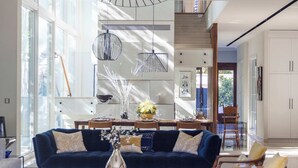 A modern living room with a dark blue sofa, a coffee table with a vase, and a dining area with a wooden table and chairs. - Carmelo  Tulip Villa (Kfar Shmaryahu)