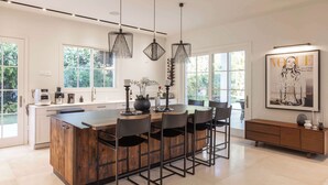 A modern kitchen with a central island, pendant lighting, and a large window. - Carmelo  Tulip Villa (Kfar Shmaryahu)