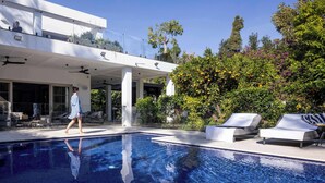 A modern pool area with a clear blue pool, lounge chairs, and a large house with a balcony overlooking the pool. - Carmelo  Tulip Villa (Kfar Shmaryahu)
