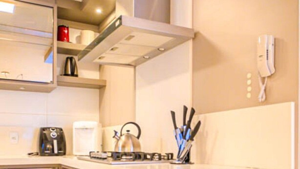 A modern kitchen with a built-in stove, kettle, and coffee maker. There are cabinets, a countertop, and a phone mounted on the wall. - Ap Alto Padrão em Jurerê a 100m da Praia (Florianópolis)