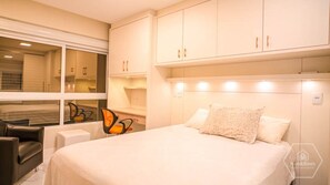 Ett hotellrum med en stor säng, ett skrivbord med en stol och ett fönster med persienner.