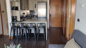 Una cocina moderna con una isla central, taburetes de bar, un sofá y una puerta de madera.