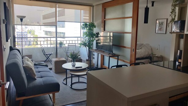 Una sala de estar moderna con un sofá, una mesa de comedor y una zona de cocina con televisor.