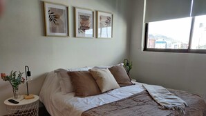 Un dormitorio con cama, mesita de noche, lámpara y una obra de arte enmarcada en la pared.