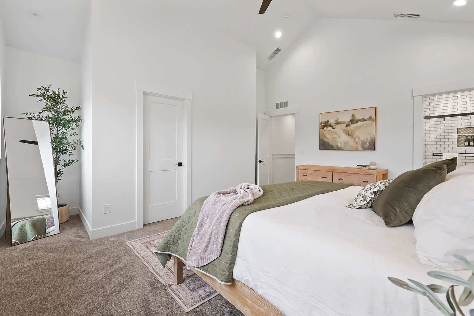 A bedroom with a bed, a dresser, a mirror, a door, and a painting on the wall.