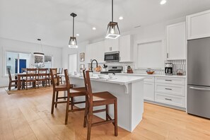 A modern kitchen with white cabinetry, a central island, and a dining area with wooden chairs.