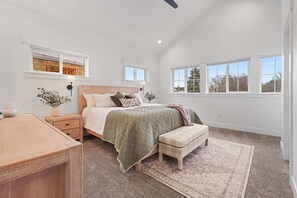 A bedroom with a bed, bedside tables, a bench, a rug, and large windows.