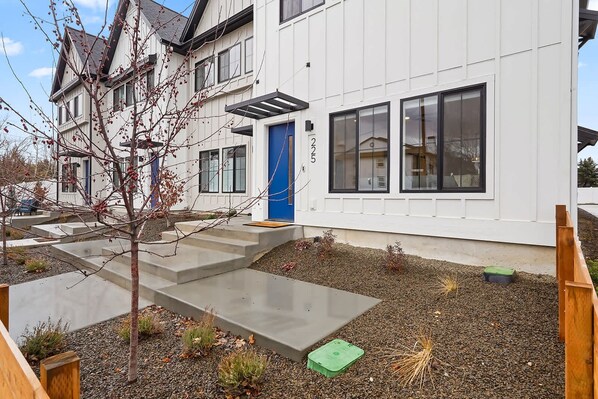 A modern two-story house with a blue door, concrete steps, and a small garden area.