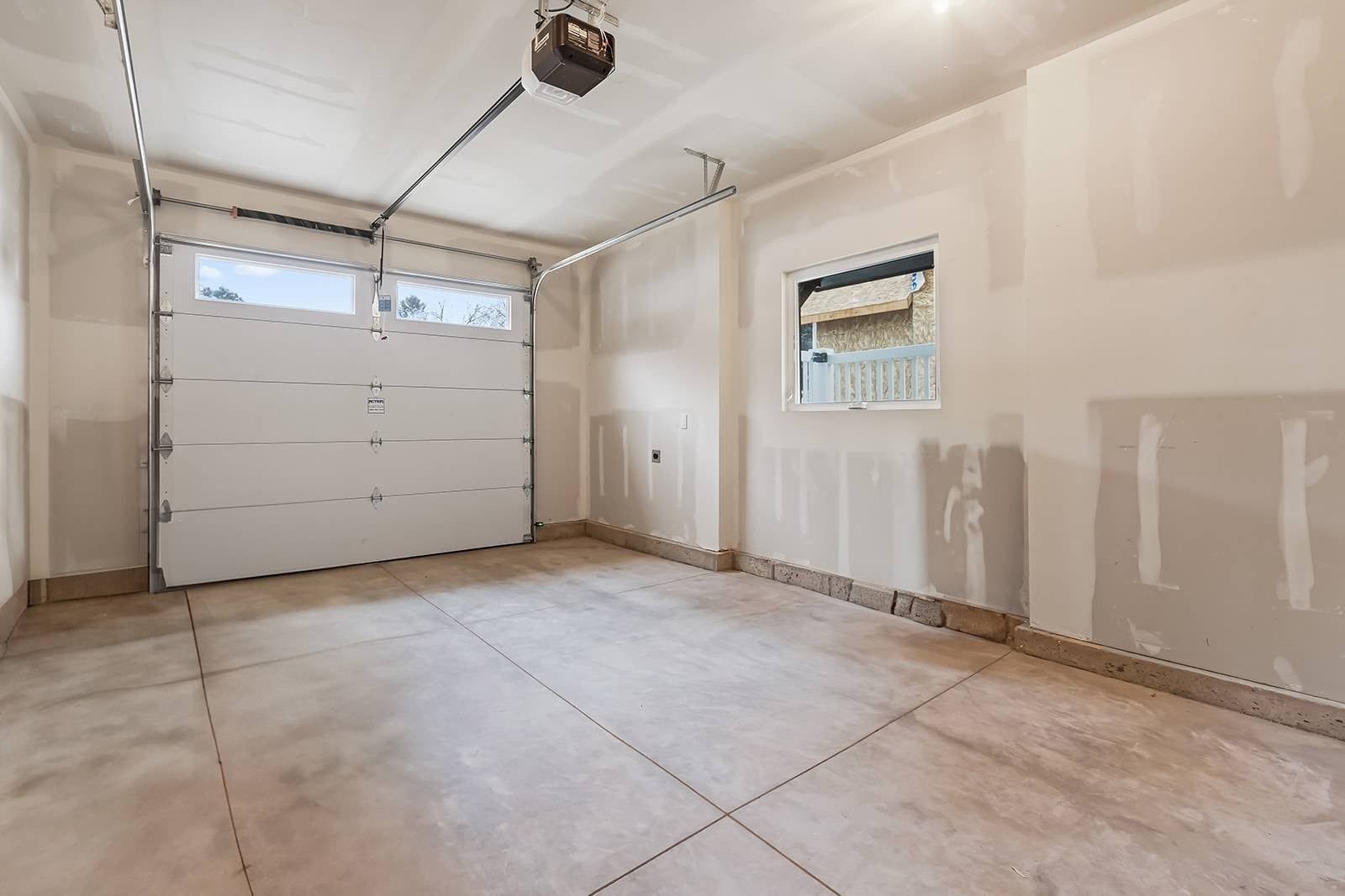 Garagem com porta branca, projetor instalado no teto e janela com vista para árvores.