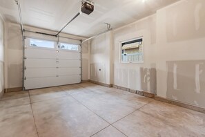 A garage with a white door, a ceiling-mounted projector, and a window with a view of trees.