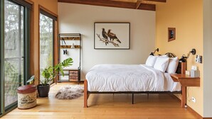 A bedroom with a large bed, wooden beams on the ceiling, a framed bird painting, and a view through large windows. - Wedge-tailed Eagle Studio (Kettering)