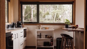 A compact kitchen with white cabinets, a countertop with a coffee maker, a toaster, and a window with a view of trees. - Wedge-tailed Eagle Studio (Kettering)