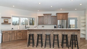 A modern kitchen with wooden cabinets, a stainless steel refrigerator, and a large island with bar stools. - Cabin getaway on 10 acres w/ wifi and fishing pond in Swan Valley (Swan Valley)