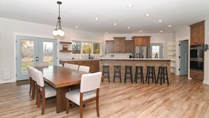 A spacious kitchen with wooden cabinets, a central island with stools, and a dining area with a wooden table and chairs. - Cabin getaway on 10 acres w/ wifi and fishing pond in Swan Valley (Swan Valley)