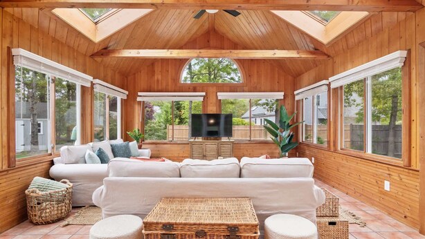 Un intérieur chaleureux en bois, avec un grand canapé, un téléviseur à écran plat et de grandes fenêtres donnant sur l’extérieur.