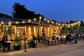 An outdoor dining area with tables and chairs, surrounded by a wooden fence and string lights.