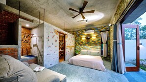 A bedroom with a brick wall, a ceiling fan, a bed, a sofa, and a small table with a book. - Outstanding  3BR villa at 50 m away from the white-sand of Hoi An beach. (phường Cẩm An)