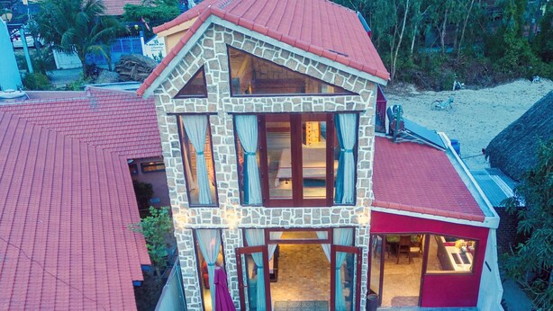 A two-story stone house with a red roof, a swimming pool, and a covered outdoor area. - Outstanding  3BR villa at 50 m away from the white-sand of Hoi An beach. (phường Cẩm An)