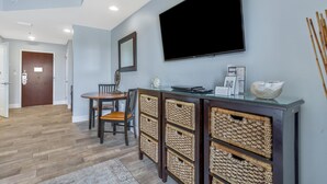 A modern living room with a flat-screen TV, a dining area with a wooden table and chairs, and a built-in entertainment unit with wicker baskets.