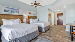 A hotel room with two beds, a ceiling fan, and artwork on the walls.