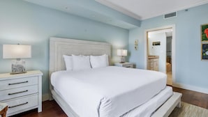 A bedroom with a large bed, white nightstands, and a door leading to a bathroom.