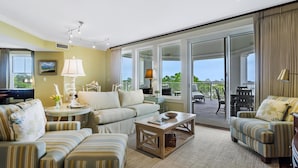 A spacious living room with a sofa, armchairs, a coffee table, and a balcony with outdoor furniture.
