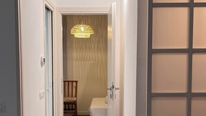 Een gang die leidt naar een slaapkamer met een bed, een stoel en een hanglamp.