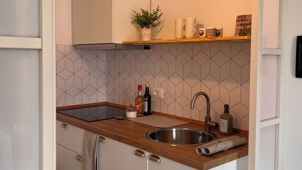 Een moderne keuken met een houten aanrecht, een roestvrijstalen spoelbak en een hangende hanglamp.