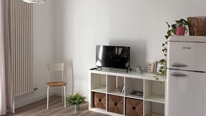 Een moderne woonkamer met een flatscreen televisie op een witte console, een witte koelkast, een houten stoel en een hanglamp.